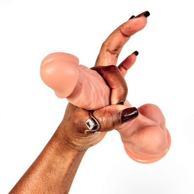 A close-up of a hand holding a realistic dildo against a plain white background.