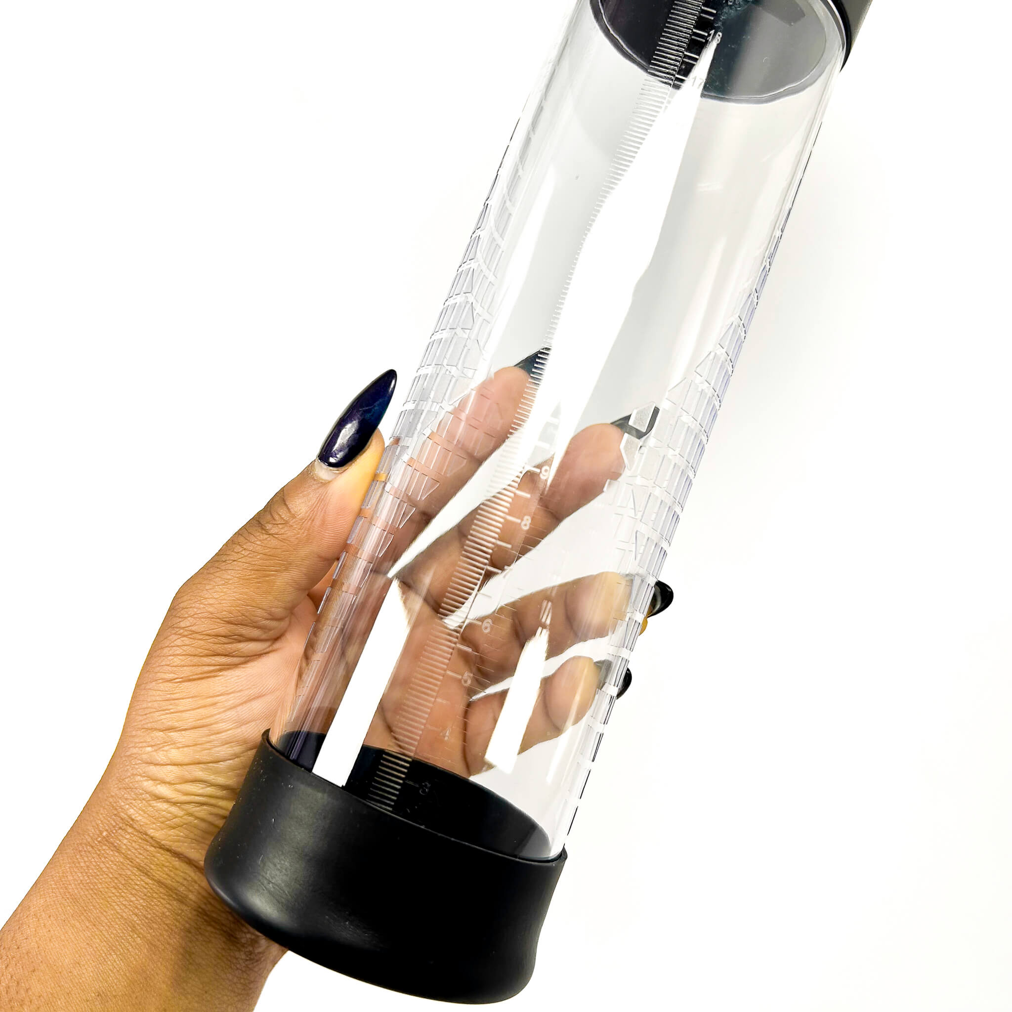 Hand holding a clear penis pump with black base on a white background