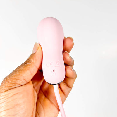 Pink insertable vibrator held in a hand against a white background