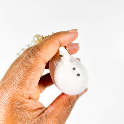 Hand holding a small white vibrator for women with a pearl necklace on a white background