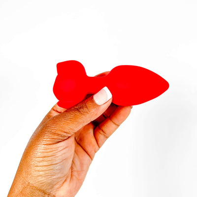 Hand holding a rose vibrating remote butt plug against a white background