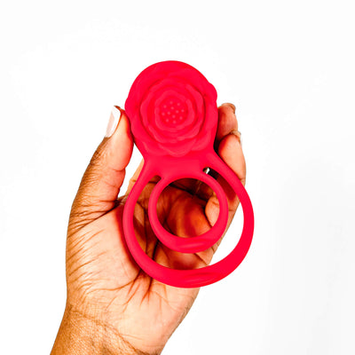 Hand holding a red siliconerose cock ring against a white background