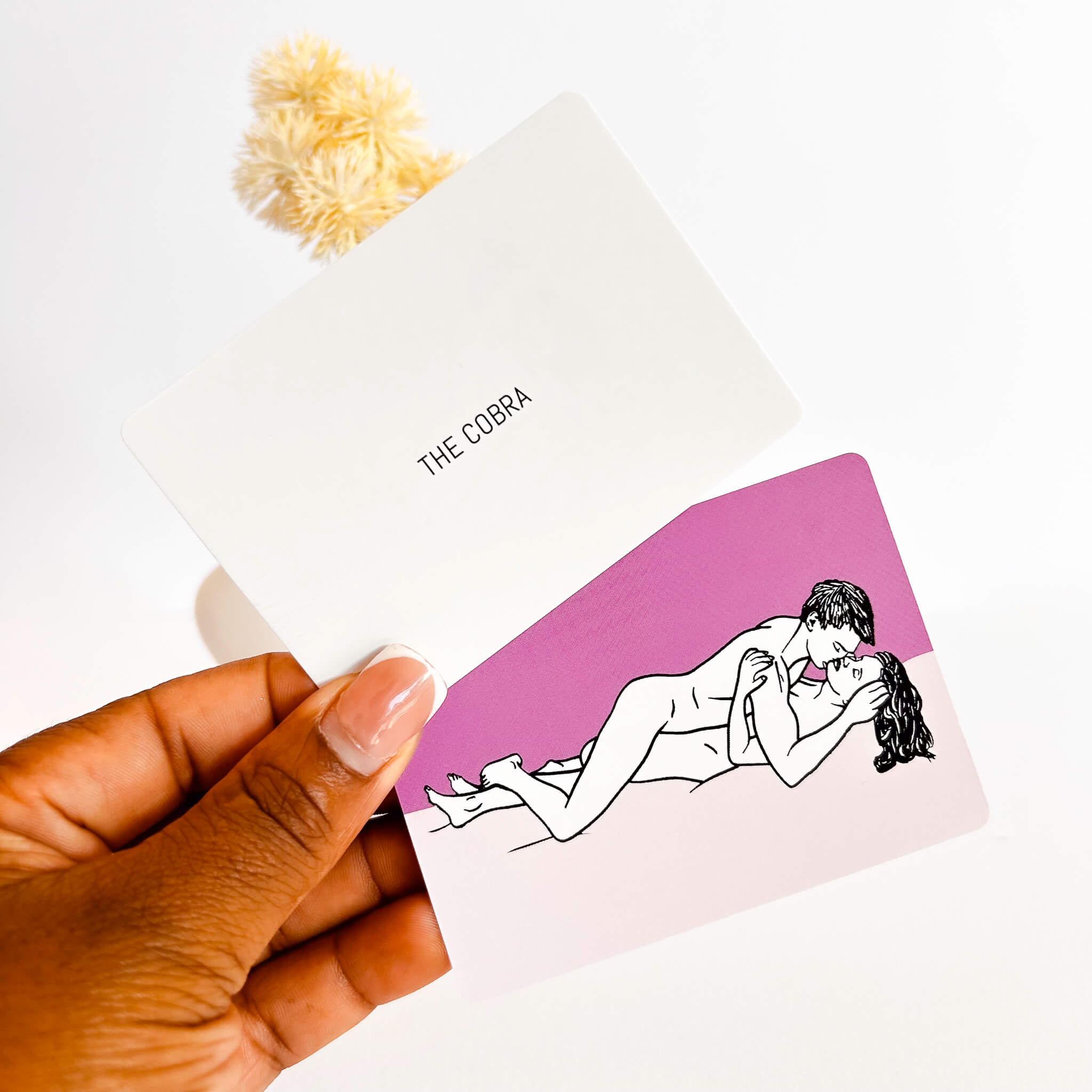 sexual position card with illustration of a couple in 'The Cobra' position held by a hand.