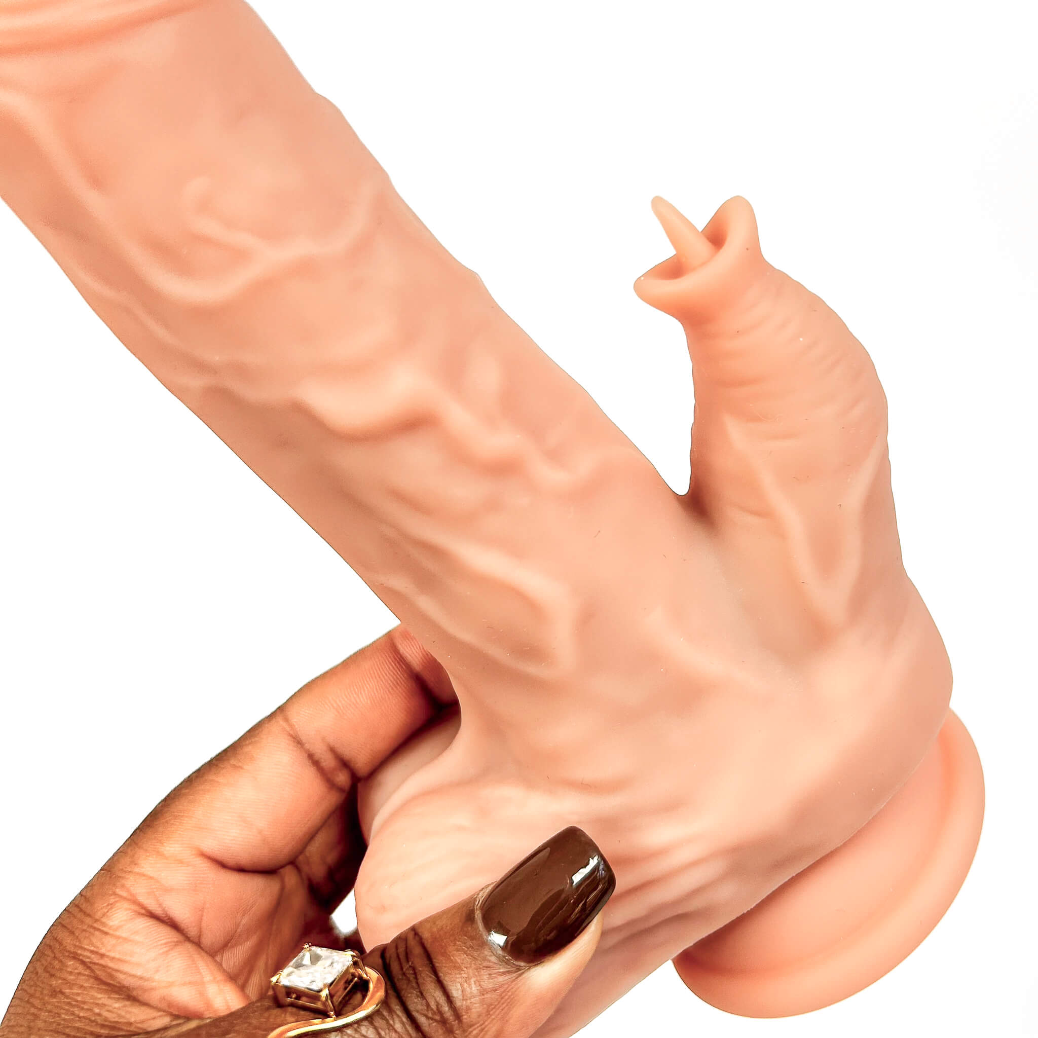A realistic flesh-toned dildo with textured detailing, shown being held by a hand with dark brown nail polish and a ring against a plain white background.