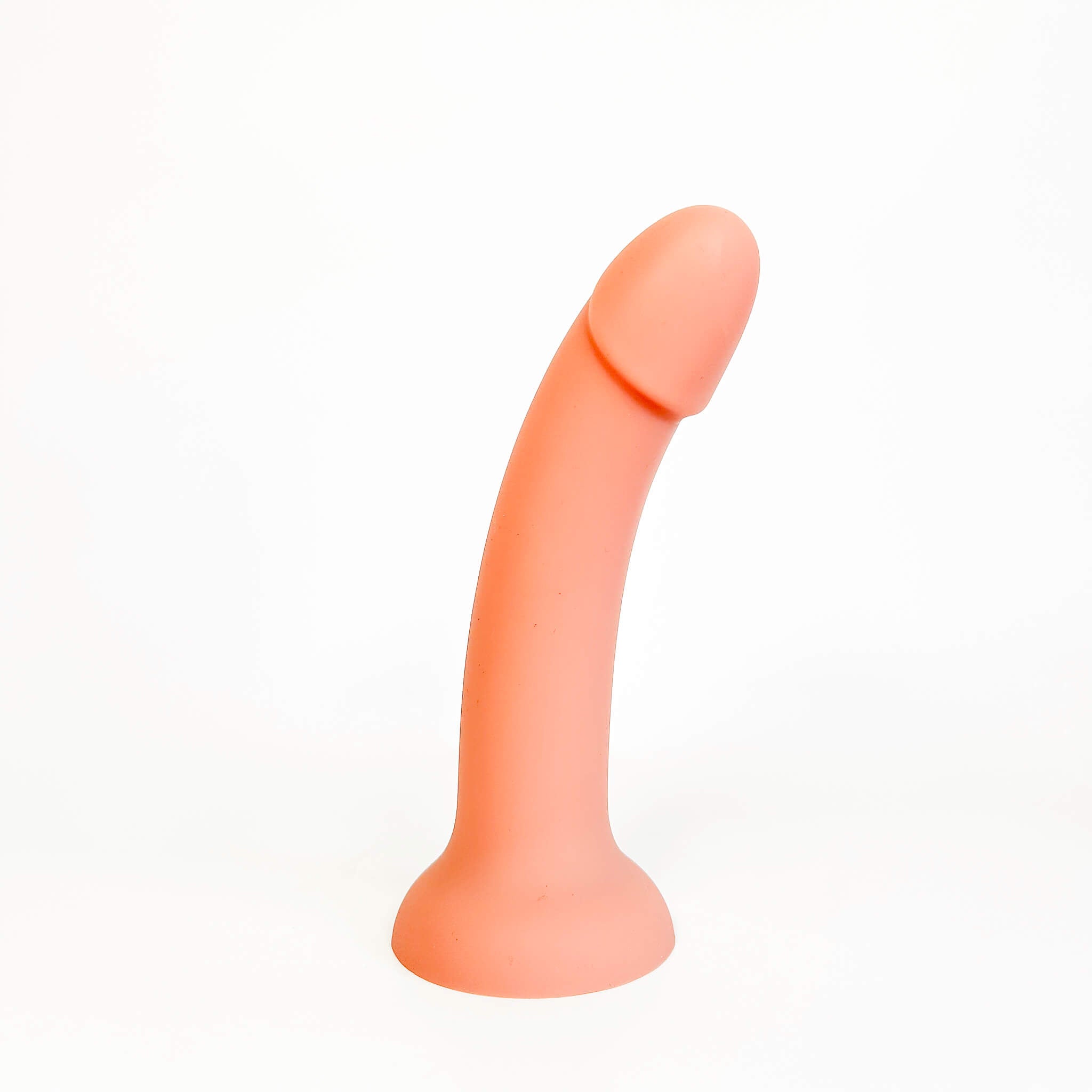 A peach-colored silicone adult novelty product, shaped like a curved penis with a flared base, photographed on a seamless white background.