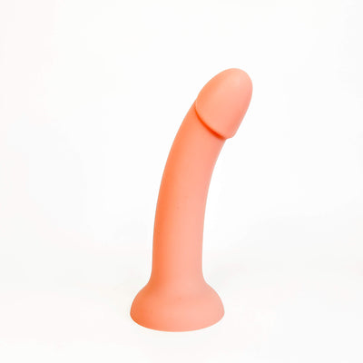 A peach-colored silicone adult novelty product, shaped like a curved penis with a flared base, photographed on a seamless white background.