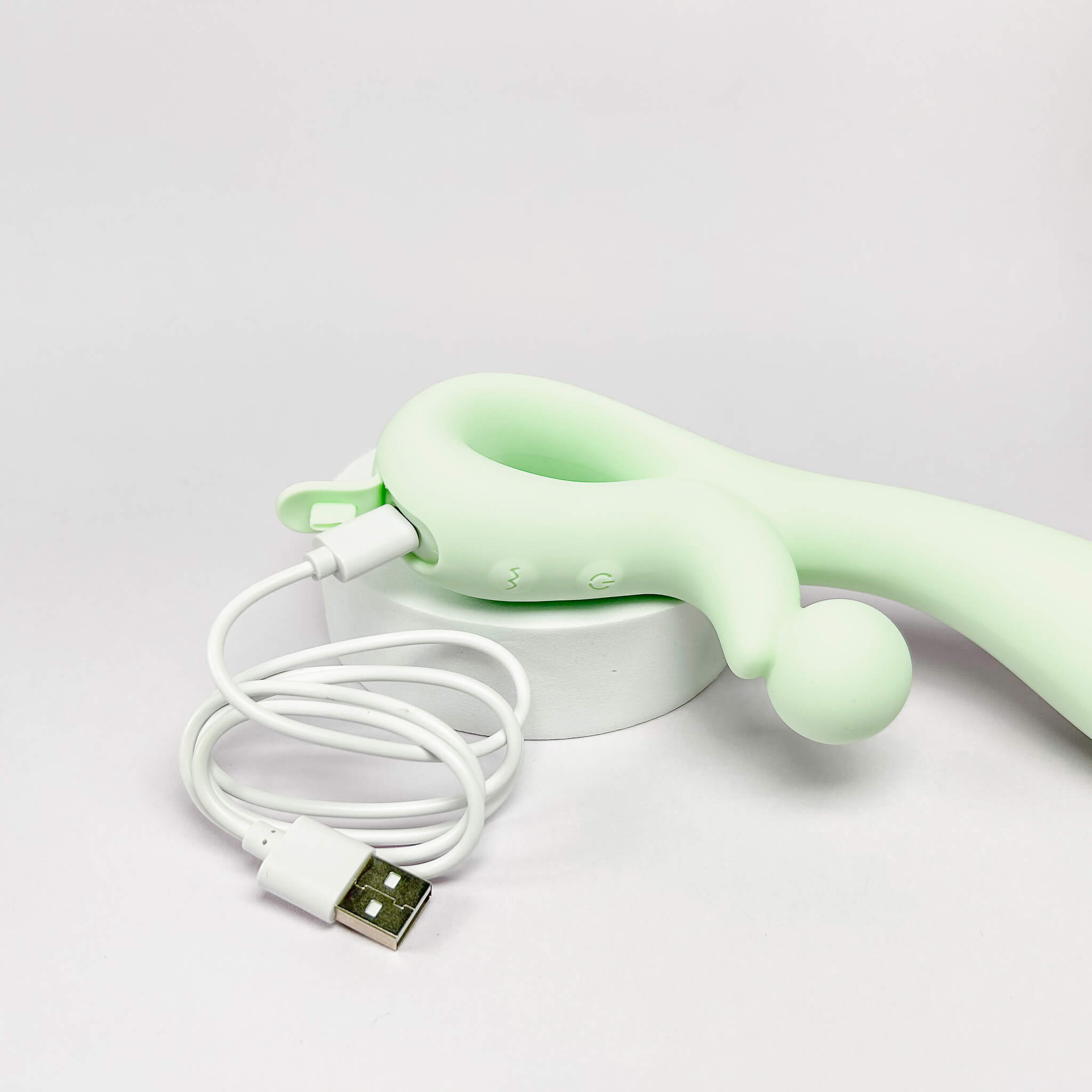 Green handheld soft silicone rabbit vibrator with USB cable on a light gray background