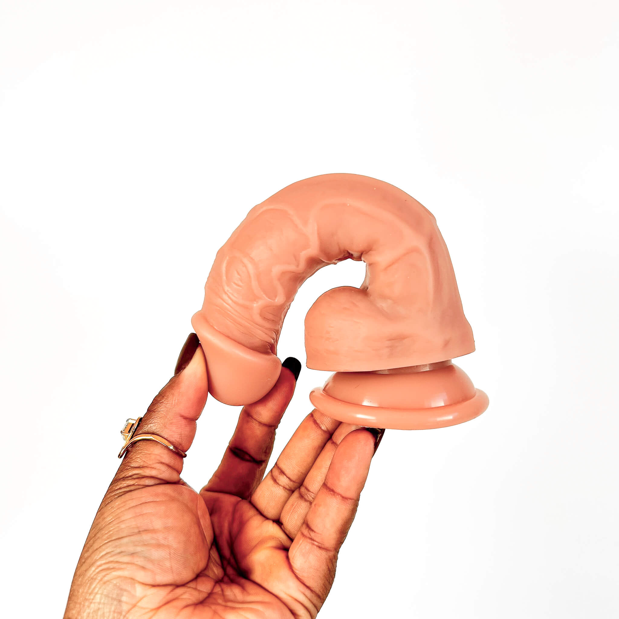 A flesh-toned silicone adult novelty item held in a person's hand against a plain white background.