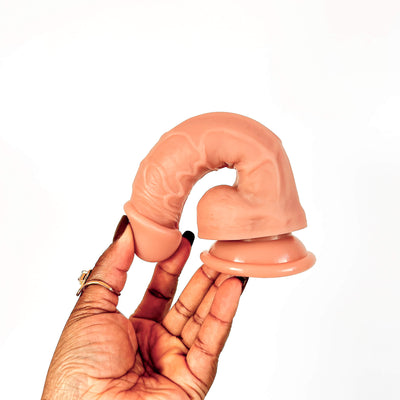 A flesh-toned silicone adult novelty item held in a person's hand against a plain white background.