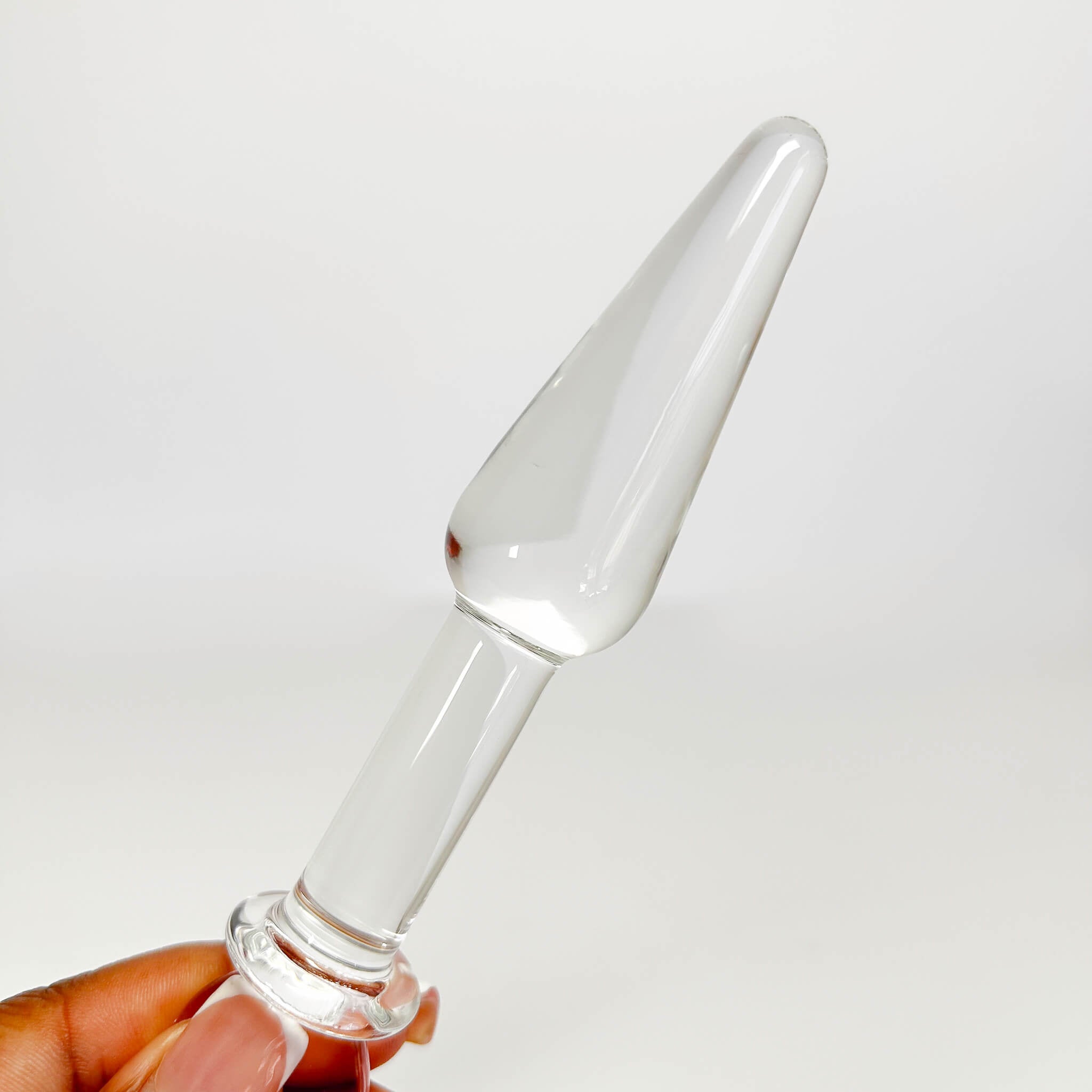 Clear tapered glass butt plug with a tapered top held by a hand against a white background