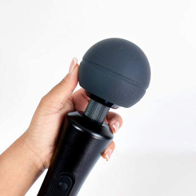 Hand holding a black wand massager with a white background