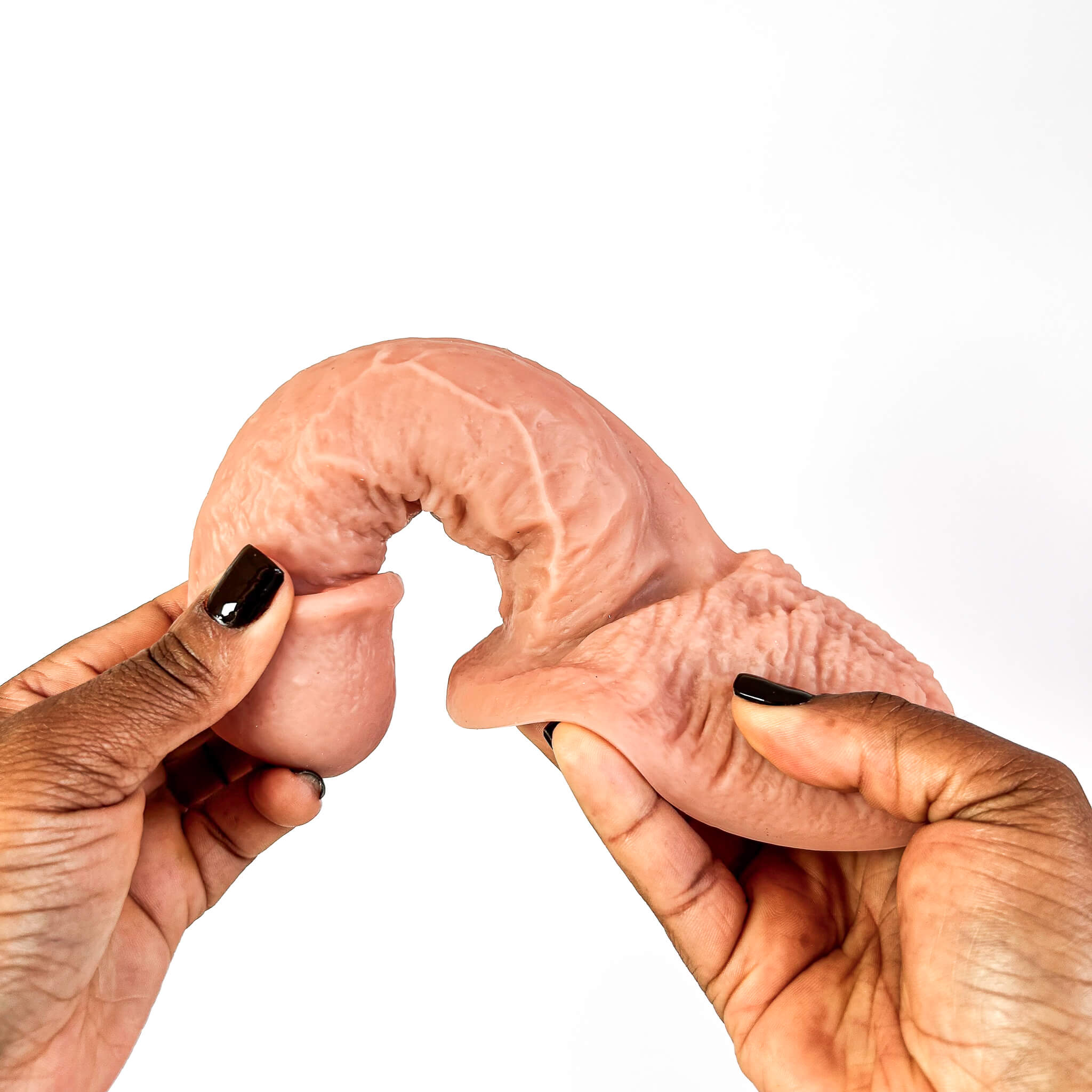 A realistic flesh-toned dildo being held between two hands with black nail polish against a plain white background.