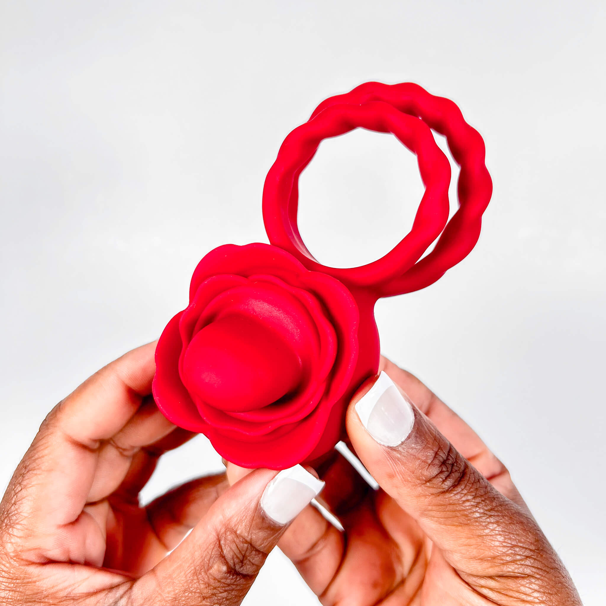 Red flower-shaped tongue cock ring held by a hand against a white background