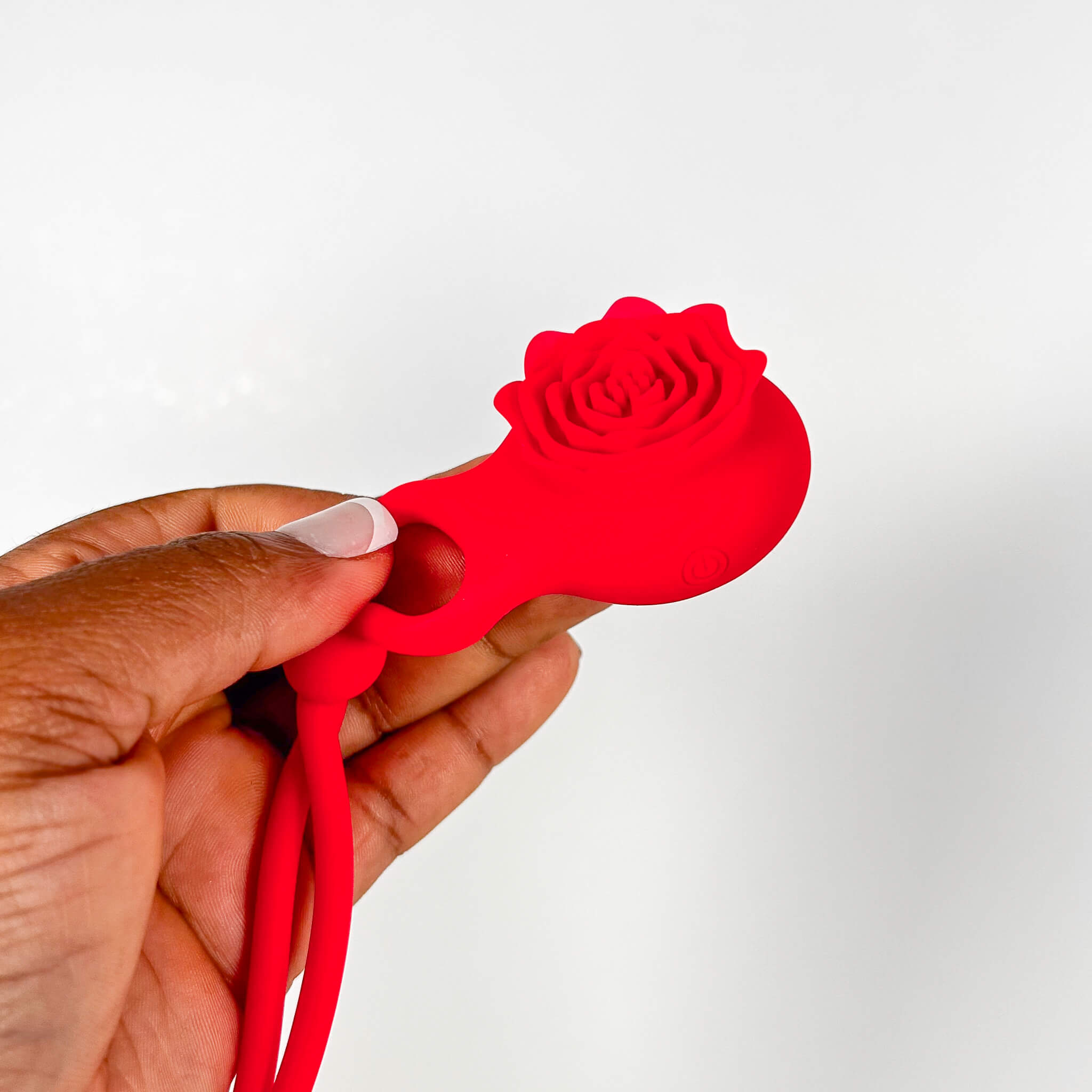 Red silicone flower-shaped vibrating adjustable cock ring held by a hand on a white background