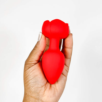 Red silicone vibrating rose butt plug held in a hand against a white background