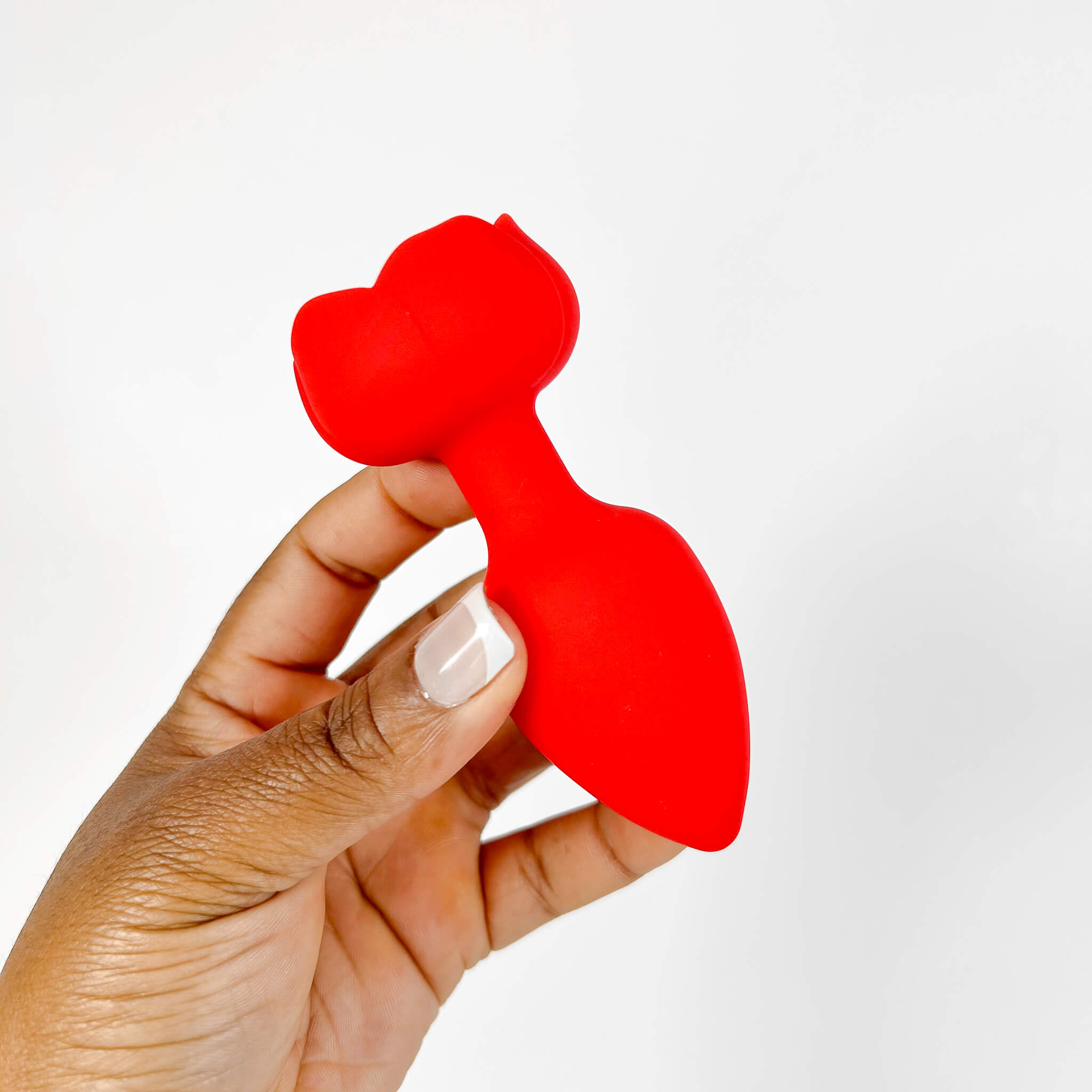Red rose-shaped butt plug held by a hand on a white background