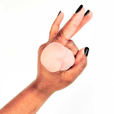 A close-up of a hand with black fingernails holding a smooth, flesh-toned silicone adult novelty item against a plain white background.
